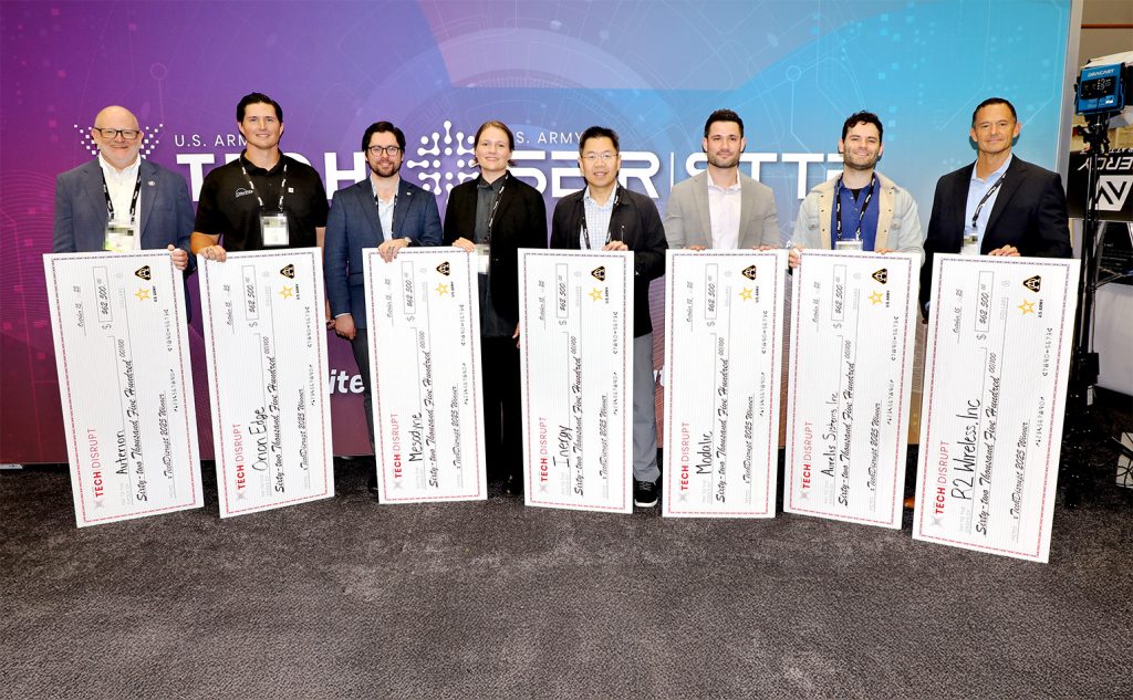 The eight xTechDisrupt winners pose with their checks following the live competition at AUSA 2025.